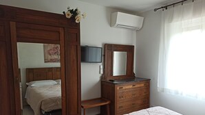 A bedroom with a wooden wardrobe, a dresser, a bed with a quilted bedspread, a flat-screen TV mounted on the wall, and an air conditioning unit. - Amaryllis vacation homes - pink house - CODE CIN: IT011002B4COYDJRPS (Romito Magra)