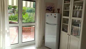 A kitchen with a refrigerator, cabinets, and a window with curtains. - Amaryllis vacation homes - pink house - CODE CIN: IT011002B4COYDJRPS (Romito Magra)