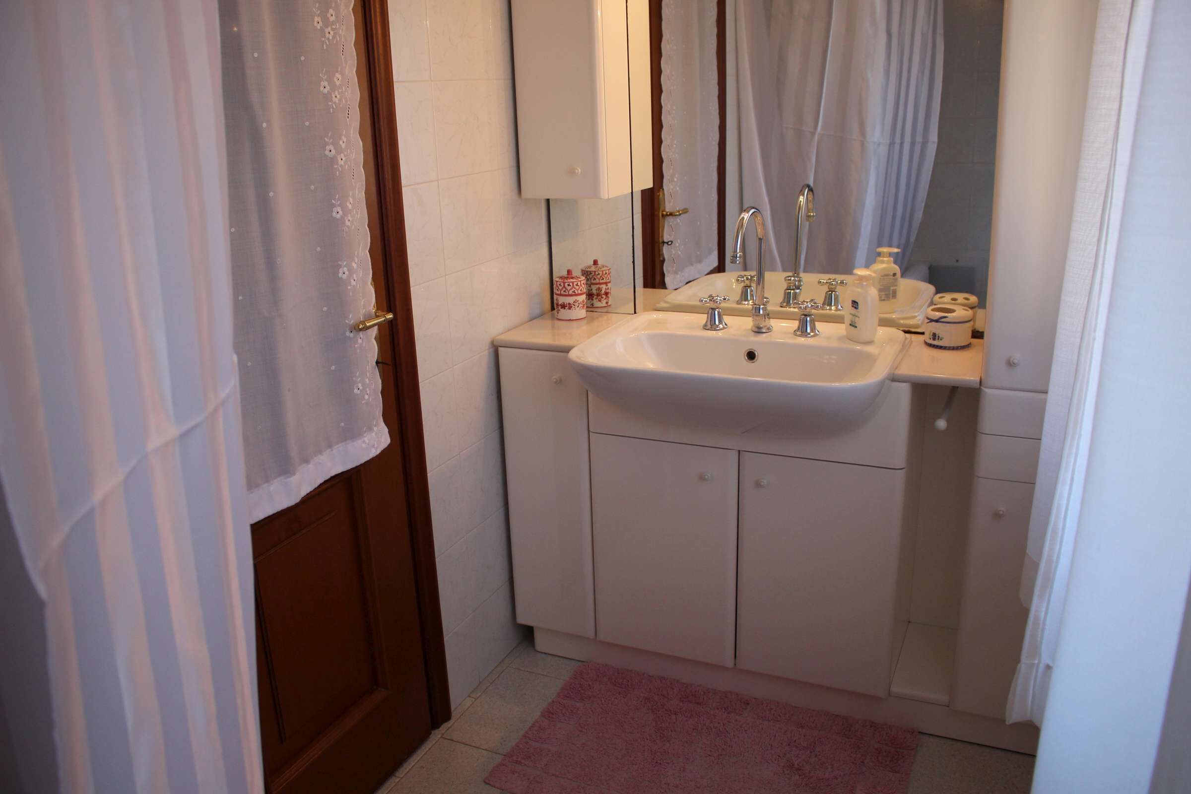 Ein Badezimmer mit Waschbecken, Spiegel und Schränken. Auf dem Boden liegt ein rosafarbenes Handtuch.