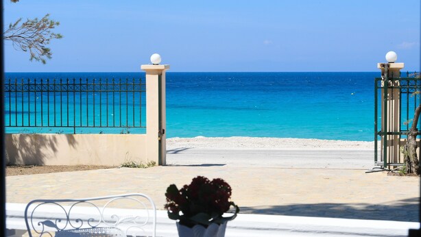 A seaside view with a white table and chairs, a potted plant, and a metal fence leading to the beach.