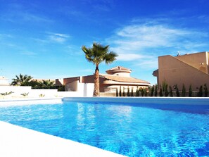 Una piscina amb aigua turquesa cristal·lina, envoltada de palmeres i un edifici amb teulada d'àmples rajoles.