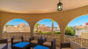 A covered outdoor seating area with wicker furniture and a view of the surrounding buildings.