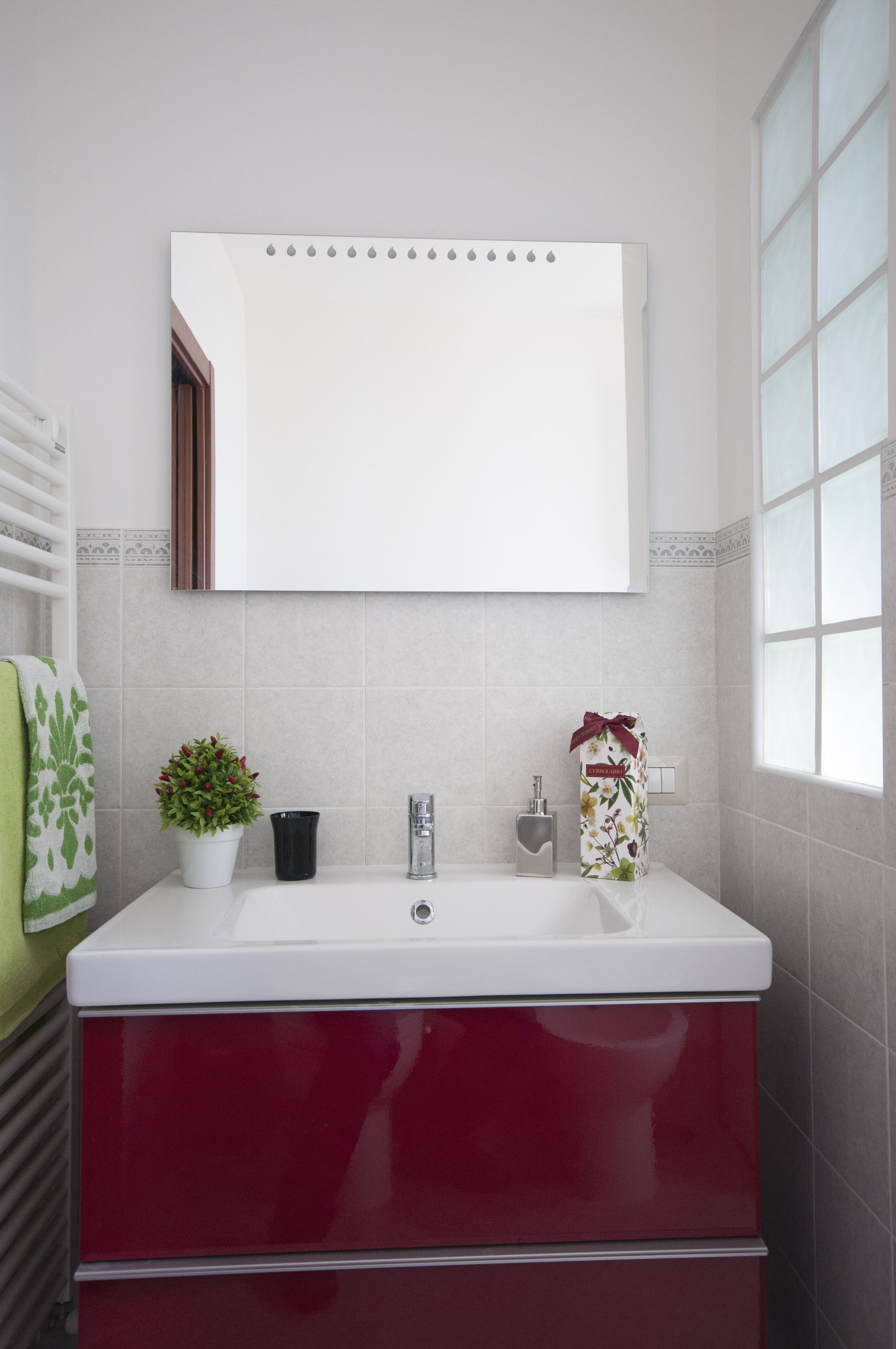 Een badkamer met een witte wastafel, een spiegel, een plant in pot en een rode kast.