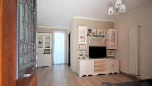 Een moderne woonkamer met een houten vloer, witte kasten, een flatscreen televisie en een grijze bank.