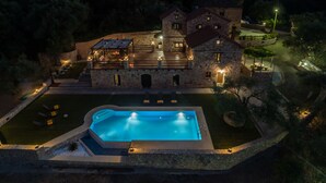 A stone villa with a swimming pool, outdoor seating, and a well-lit patio area.