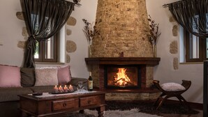 A cozy living room with a stone fireplace, a wooden coffee table, a sofa with cushions, and a chair.