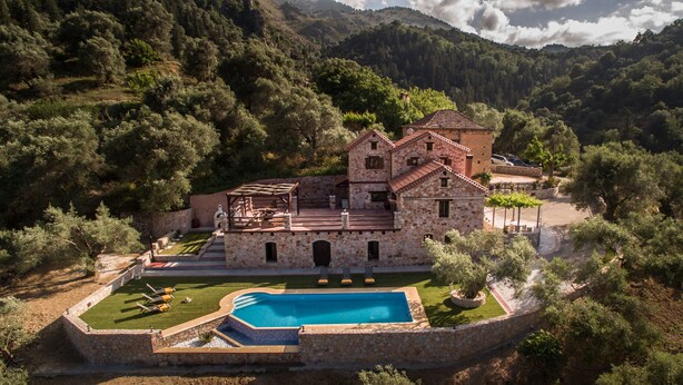 A stone building with a swimming pool, surrounded by trees and hills.