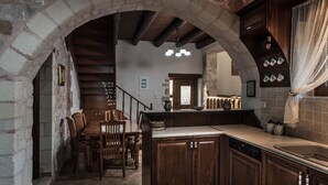 A rustic kitchen with stone arches, wooden cabinets, and a dining area with a wooden table and chairs.
