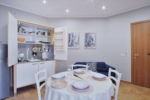 A compact kitchen with white cabinets, a dining table set for four, and a blue sofa in the background.