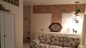 Une pièce avec un canapé à motifs floraux, une armoire blanche, un miroir et un mur en briques.