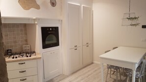 Une cuisine compacte équipée d’une cuisinière à gaz, d’un four, de meubles blancs et d’une table à manger avec des chaises.