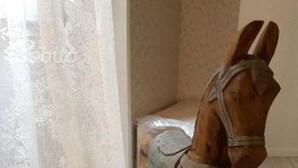 Un cheval à bascule en bois, dans une pièce décorée d’un rideau en dentelle blanche et dotée d’un plancher de couleur claire.