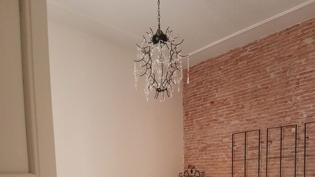 Une chambre avec un mur en briques, un lustre, un lit recouvert d’une courtepointe bleu clair, deux serviettes pliées, un panier en osier et une cage à oiseaux en métal.