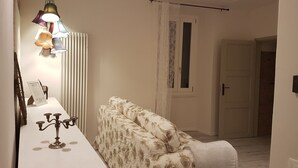 Un couloir avec un canapé à motifs floraux, une table blanche surmontée d’un chandelier et une lampe suspendue.