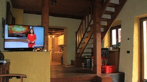 Ett rymligt vardagsrum med en trätrappa, en tv och ett kök i bakgrunden.