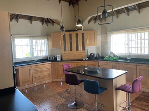 A modern kitchen with wooden cabinets, a central island with bar stools, and pendant lighting. - A superb 3-bedrooms Holiday Villa, mins away from Ocho Rios vibrant Town Centre (Tower Isle)