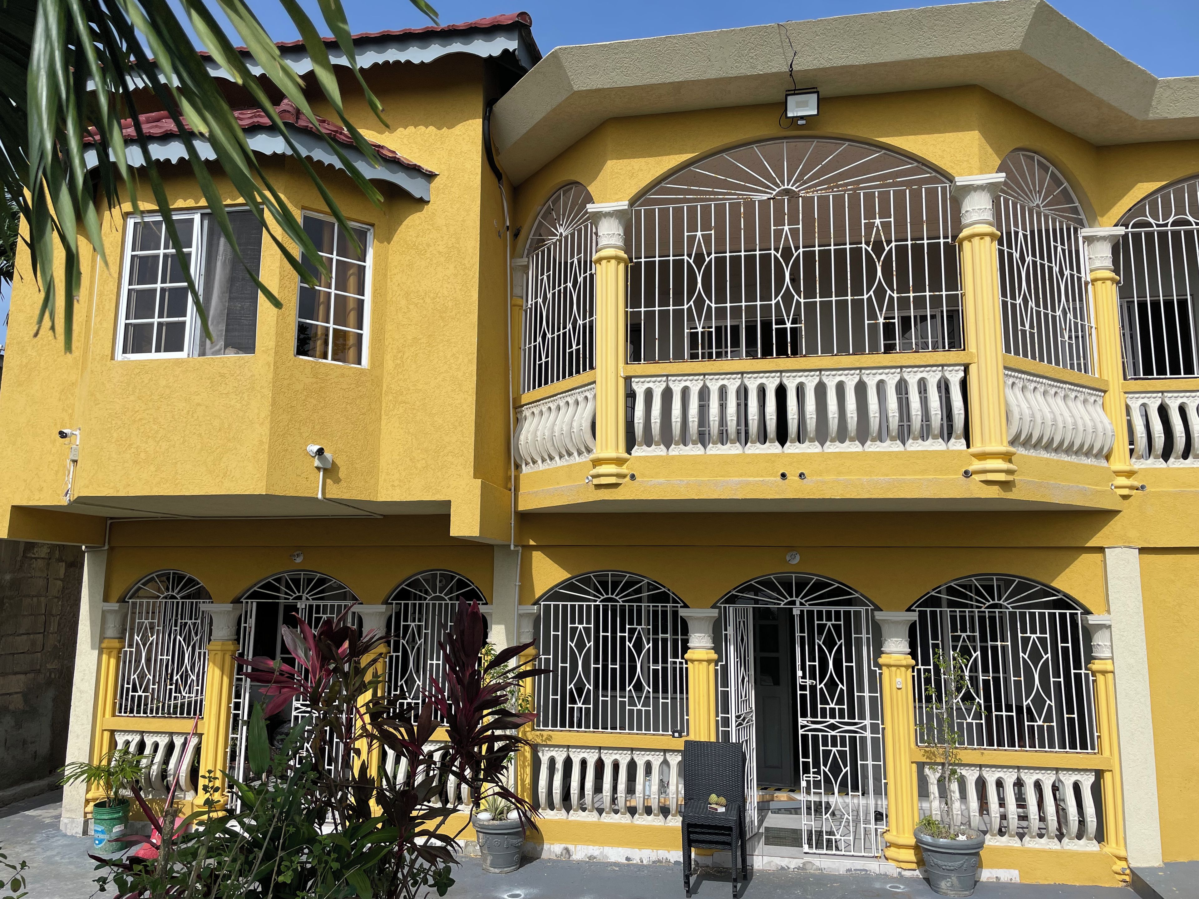 A yellow building with barred windows and balconies, a door, and potted plants.