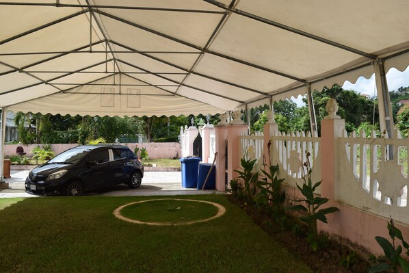 A covered parking area with a car, a small lawn, and a white fence.