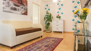 Una sala de estar con un sofá blanco, un tapete estampado, una mesa de centro de vidrio con jarrones, y un cuadro de una cascada en la pared.