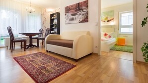 Una sala de estar con un sofá, una mesa de comedor con sillas, una estantería y un cuadro en la pared.