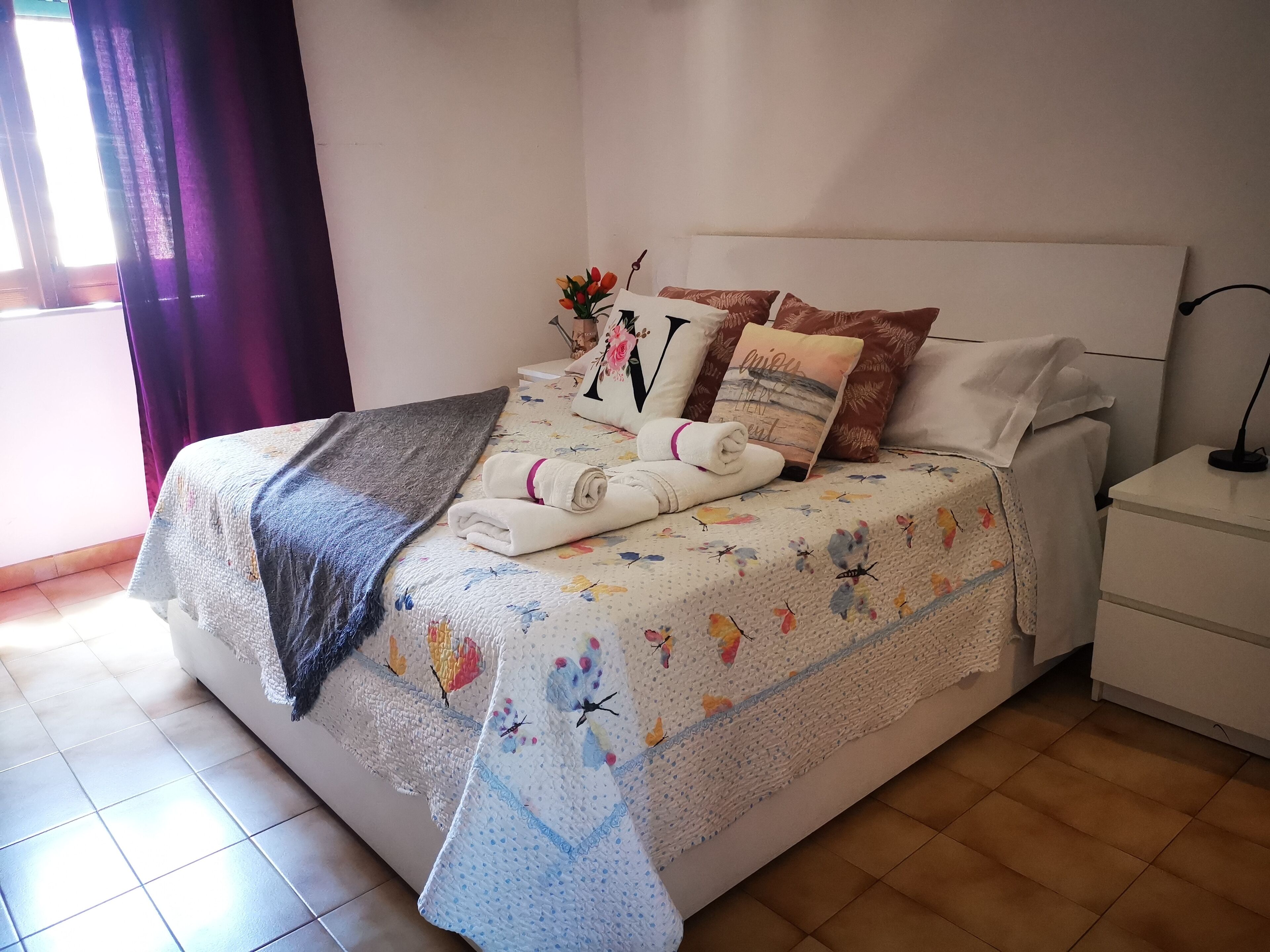 Un lit bien fait, avec une couvre-lit à motifs floraux, deux oreillers et une serviette pliée.