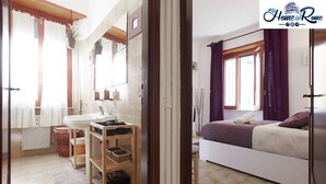 Un dormitorio con cama, ventana con cortinas, mesita de noche y un pequeño mueble auxiliar.