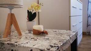 Una habitación con una mesa cubierta por un mantel con tiras cómicas, un refrigerador blanco, una lámpara con base de madera y un jarrón con flores amarillas.