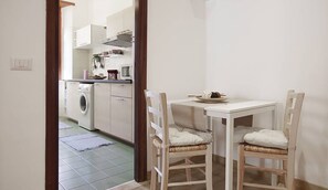 Une cuisine compacte comprenant un lave-linge, une table à manger avec deux chaises et un petit meuble de rangement.