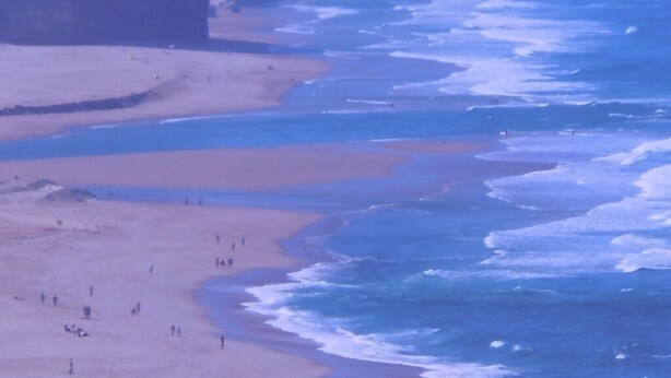 Une plage où des personnes se promènent le long du rivage, avec des falaises en arrière-plan.