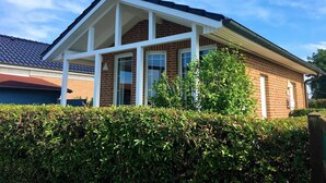 A two-story house with a brick facade, white window frames, and a covered porch. - Family-friendly house with dunes, view of ocean, sauna (Lübeck)