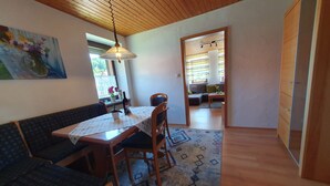 A dining area with a wooden table and chairs, a patterned rug, and a painting on the wall.