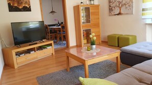 A living room with a television, wooden furniture, a dining area, and a painting on the wall.