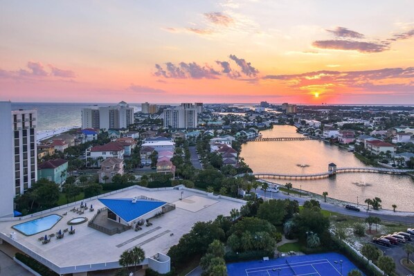 Un paisaje urbano costero al atardecer con un puerto deportivo, edificios residenciales y una gran piscina.