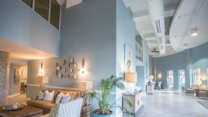 A spacious living area with a high ceiling, a large blue potted plant, and a sofa with patterned cushions.
