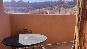 A balcony with a round metal table and chairs, overlooking a desert landscape with mountains in the background. - 1A4 Shared Pool, Private Patio, Garage, Close to Arches (Moab)