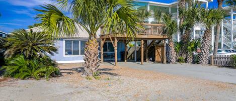 A beachfront property with a wooden deck, palm trees, and a clear blue sky.