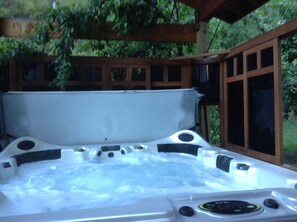 A hot tub with a wooden deck and glass panels, surrounded by greenery. - Canyon Loft. Not Too Far, Not Too Close. Private Stay.  STR # 000795 (Leavenworth)