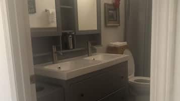 Een badkamer met een wastafel met dubbele wastafels, een toilet en een douchegordijn.