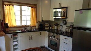 Una cocina compacta con armarios blancos, horno de acero inoxidable, microondas y refrigerador.