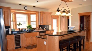 Una cocina amplia con armarios de madera, una isla central con taburetes de bar, lavavajillas y un amplio ventanal que proporciona luz natural.