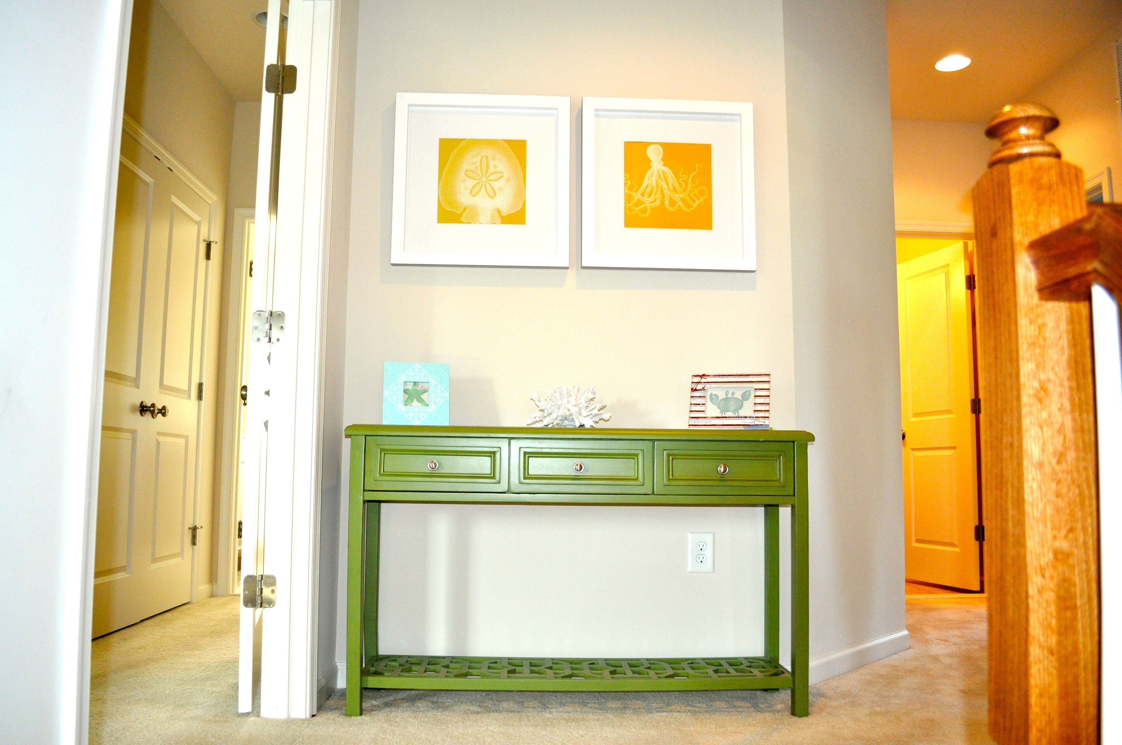A hallway with a green console table, two framed pictures on the wall, and a door at the end.