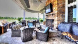 A covered patio area with wicker furniture, a brick fireplace, and a television mounted on the wall.