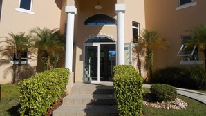 A building with a beige facade, a central arched entrance, and palm trees in the foreground.