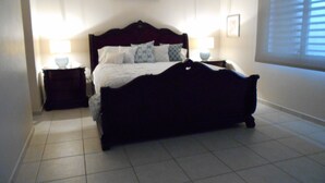 A bedroom with a large bed, two bedside tables with lamps, a ceiling fan, and a window with blinds.