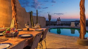 Un espacio de comedor al aire libre con piscina, sillas de madera y una mesa preparada para dos.