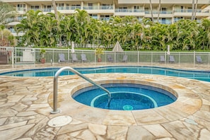 A circular hot tub with a stone surround, surrounded by lounge chairs and a white fence. - Experience paradise in our cozy 2 bedroom condo near the beach (Kihei)