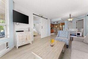 A modern living room with a flat-screen TV, a patterned sofa, and a coffee table. - Experience paradise in our cozy 2 bedroom condo near the beach (Kihei)