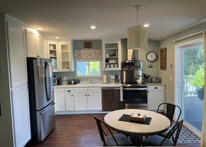 A modern kitchen with white cabinetry, stainless steel appliances, a round dining table, and a view of the outdoors.