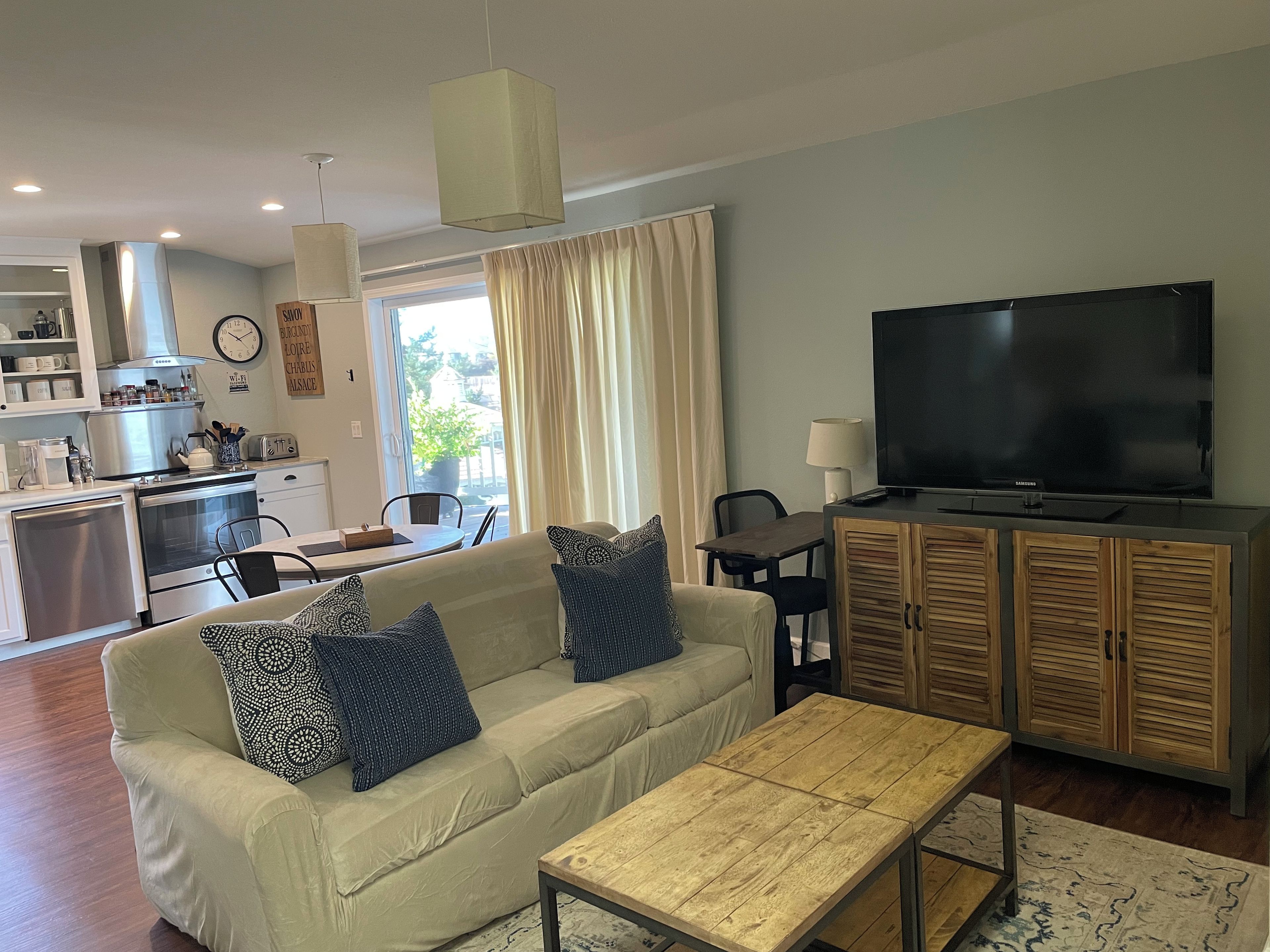 Una sala de estar con sofá, mesa de centro, televisor y una cocina al fondo.