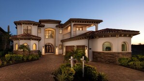 Una casa grande de varios pisos con fachada simétrica, ventanas arqueadas y una entrada central con camino de acceso portón.